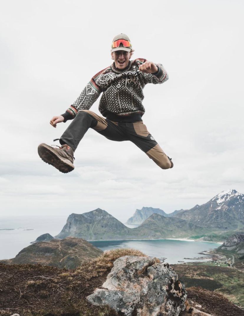 Ådne Birkeland jumping on a mountain in Lofoten wearing a knitted 1994 Olympic sweater